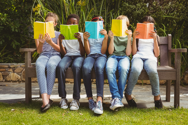 Children sitting in row and reading books at the park